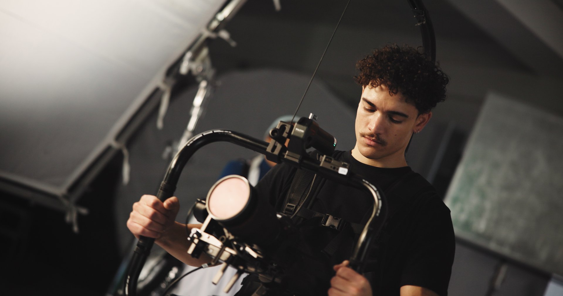 Man, filming and cameraman with stabilizer in studio of broadcast, production process and record. Person, tech and cinematographer on set for shooting news, documentary footage and rehearsal of media