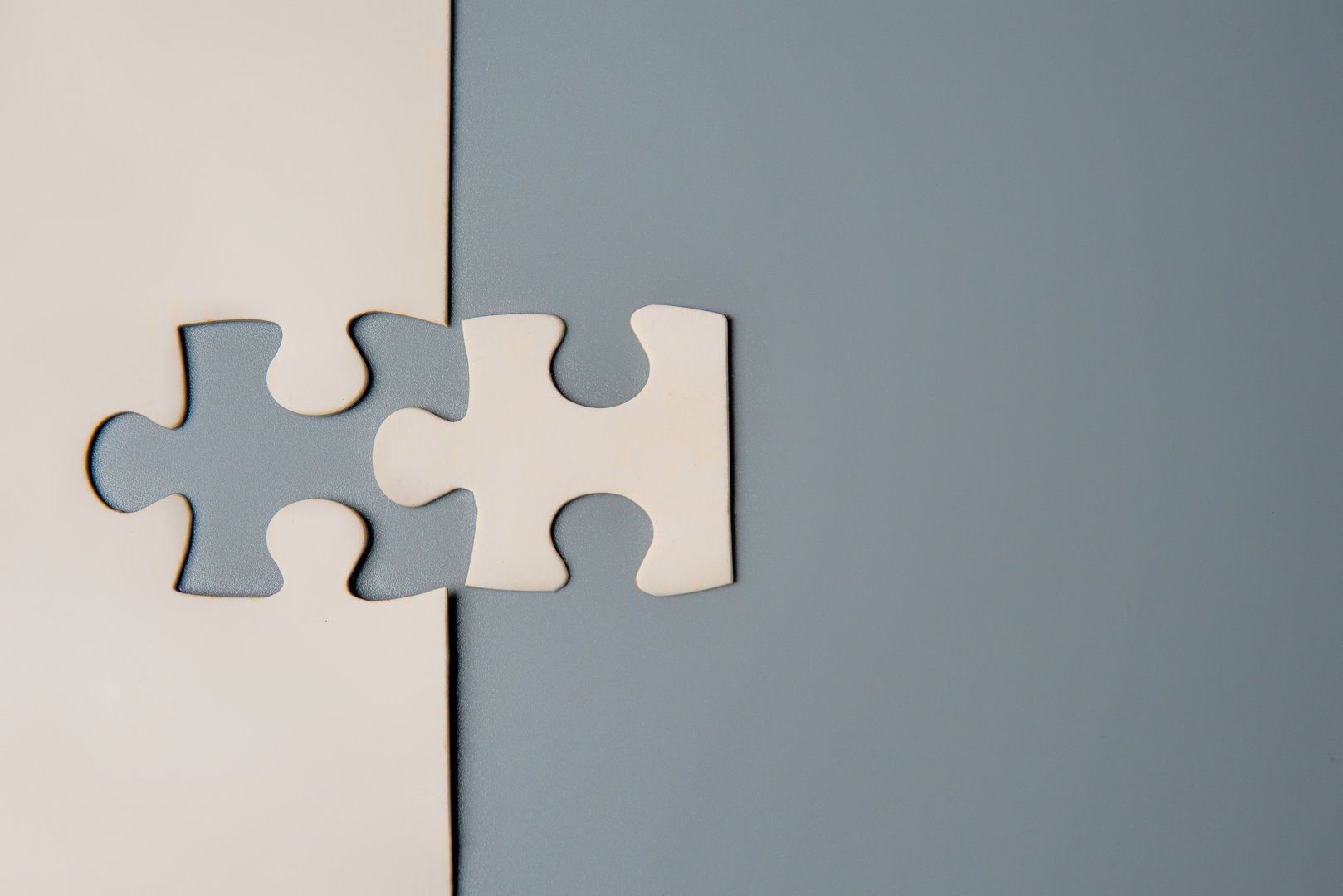 Two puzzle pieces connecting, one white and one grey, on a contrasting background, symbolizing unity, connection, and collaboration. Copy space for text.