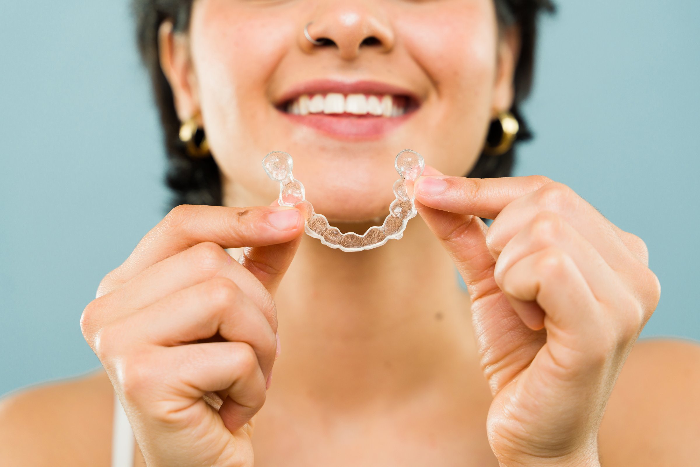 Portrait of a young woman smiling while holding a transparent teeth aligner in a studio, seen up close