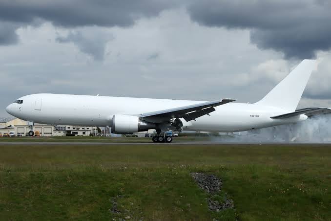 White cargo plane landing on a runway with smoke from its wheels, under a cloudy sky.