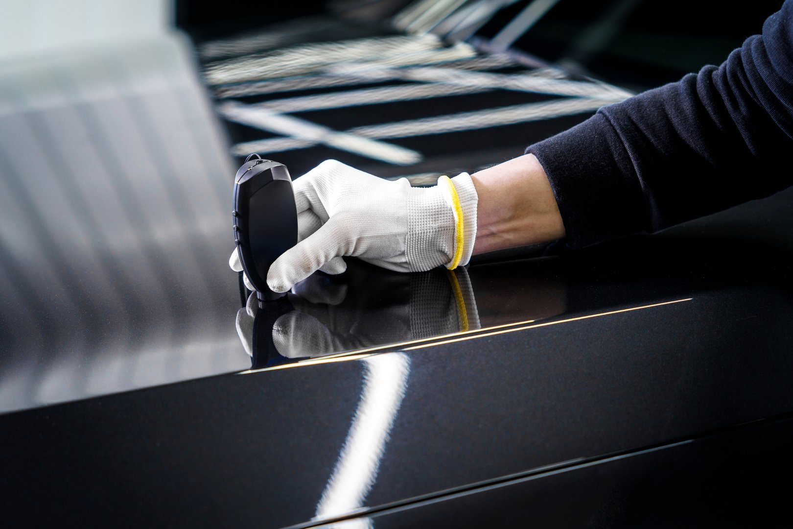 Technician measures car paint thickness with a specialized device on glossy black surface, ensuring quality and uniformity in automotive finishing