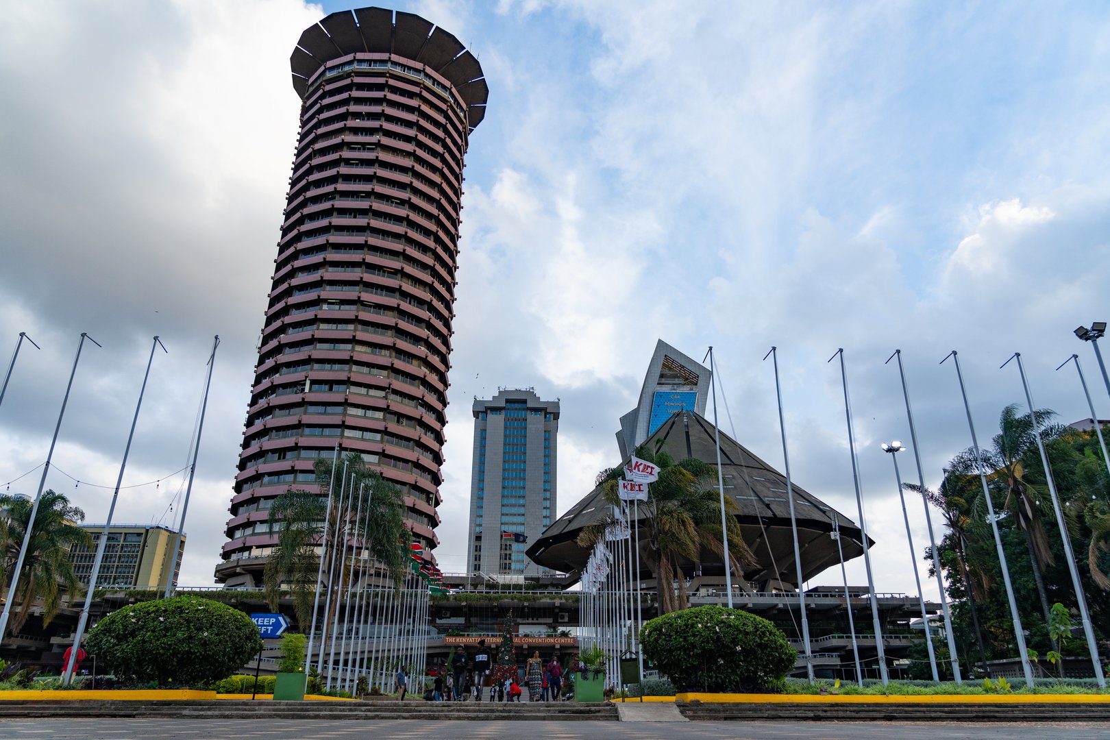 A front view of the Kenyatta International Convention Centre (KICC) in Nairobi, Kenya, taken on December 22, 2024. The iconic cylindrical tower stands prominently in the background, framed by the entry gate and surrounding gardens. KICC is a key landmark and a major hub for conferences and events in East Africa.