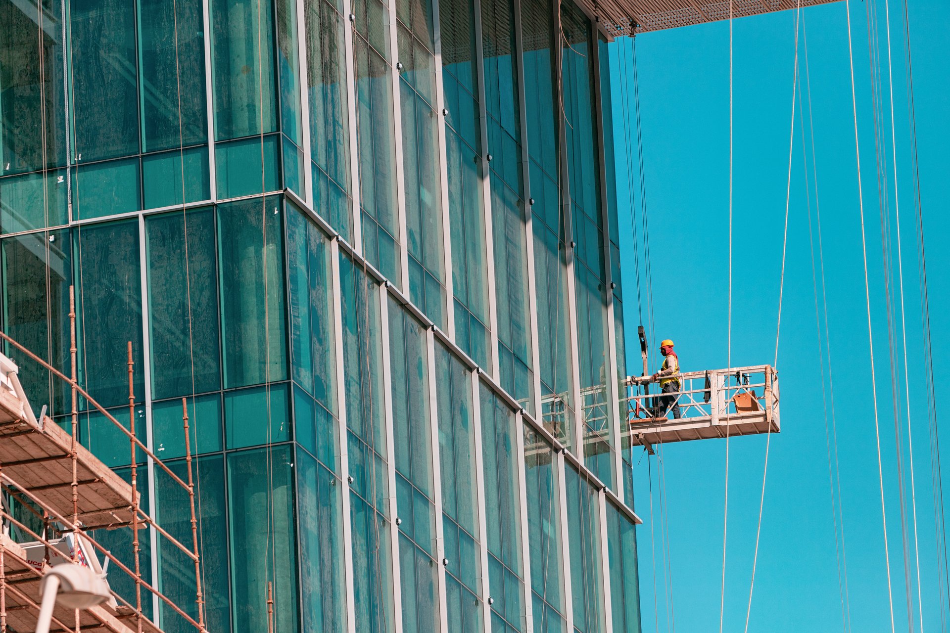 21 January 2025, Abu Dhabi, UAE: Construction worker standing on suspended platform cleaning windows of modern glass skyscraper