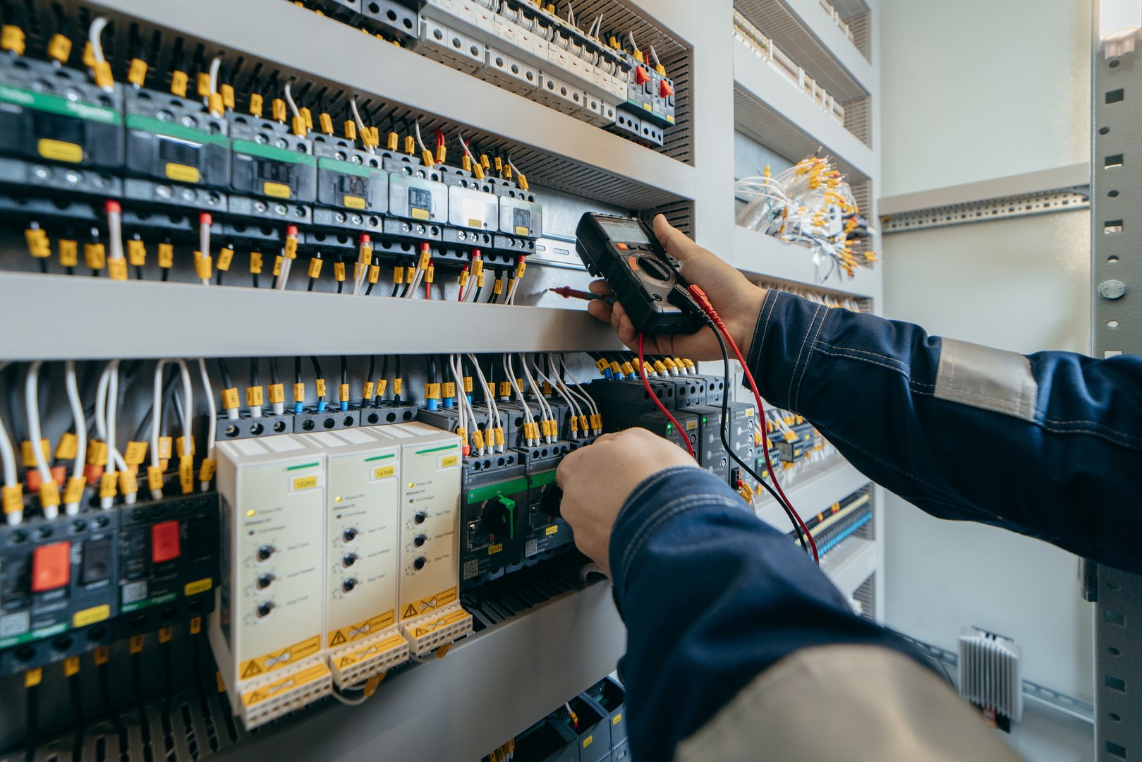 Electrician builder engineer testing and screwing equipment in fuse box and repairing of modern electricity power station using voltmeter. Automatic control cabinet