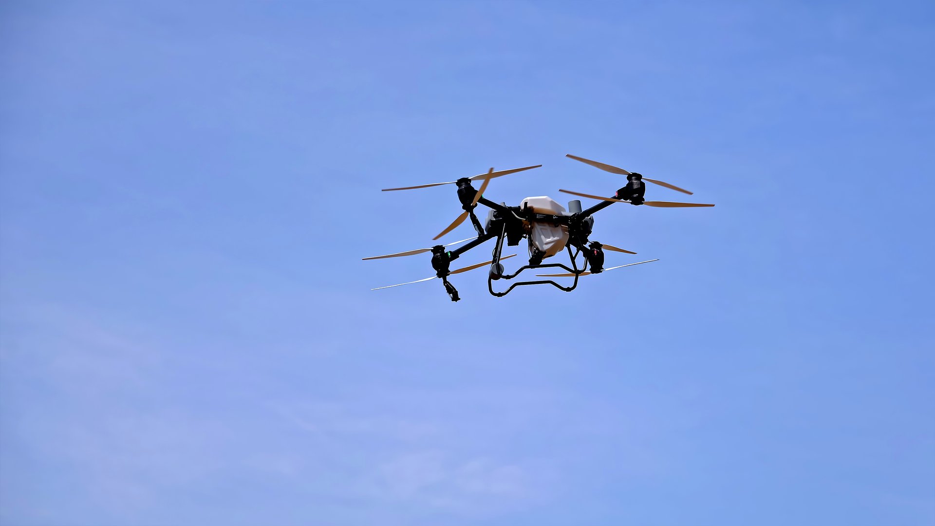 Industrial drone flying in clear blue sky. An agricultural drone equipped with multiple rotors is flying in the sky, used for crop monitoring, spraying, or farm management.
