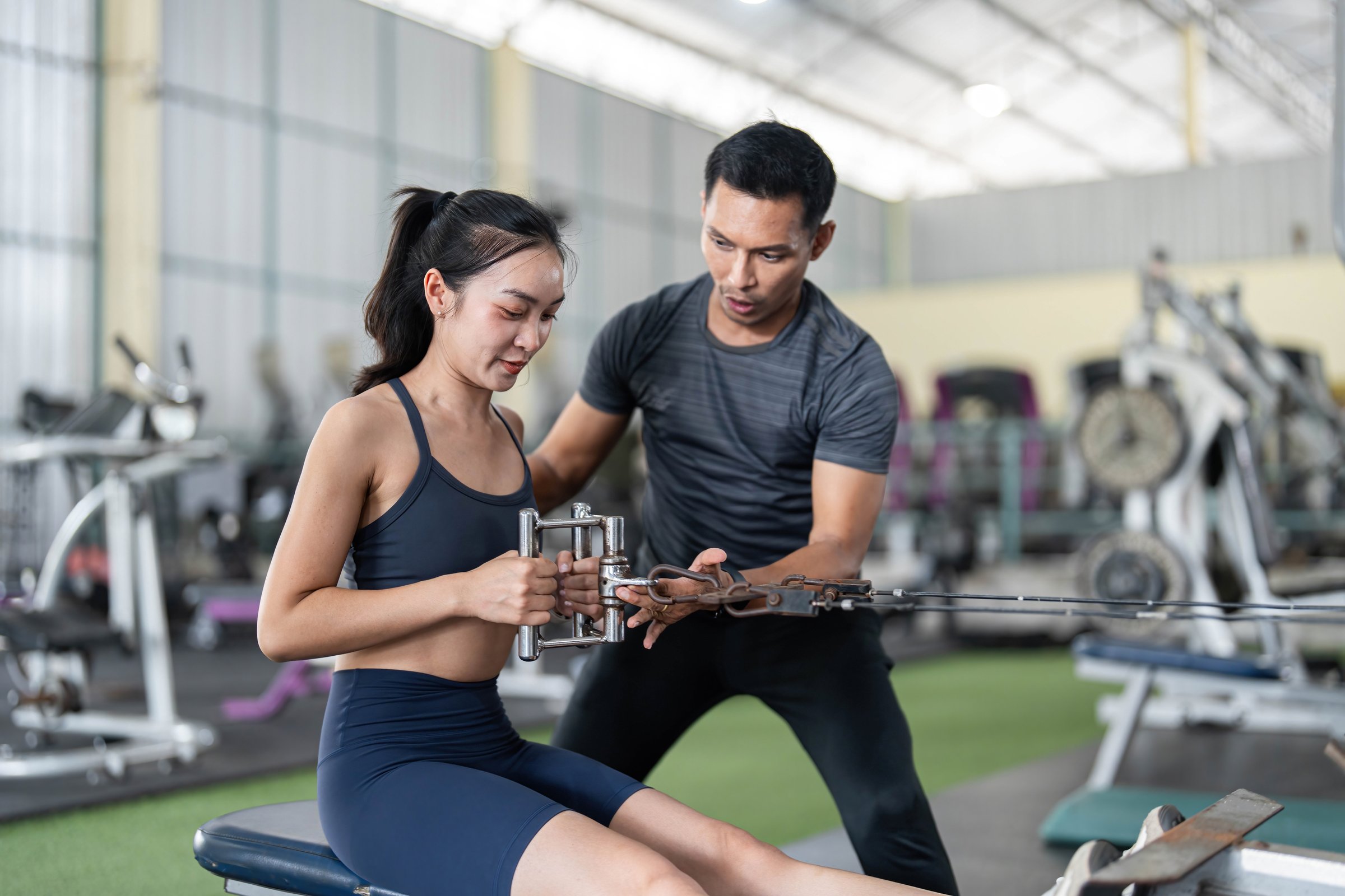 A fitness trainer helps a woman with cable machine exercises, enhancing strength and fitness in a supportive gym environment.