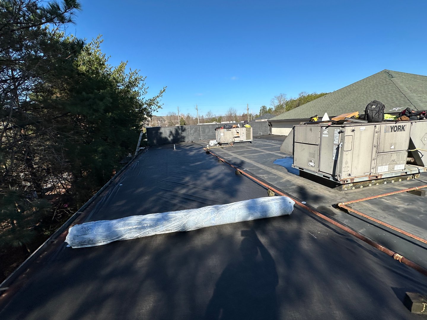 Two construction workers install a black waterproofing membrane and asphalt bitumen shingle on a flat roof, while another worker stands nearby on top of the building