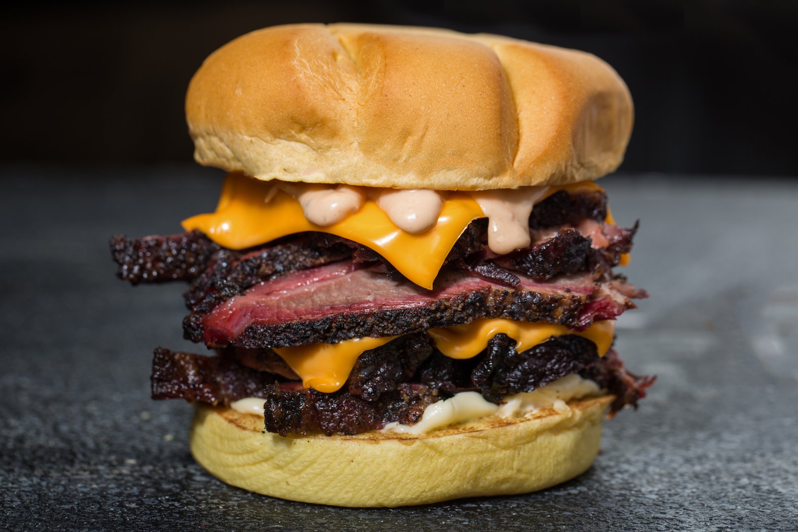 Double Beef Brisket Sandwich or burger with melted cheese and mayonnaise isolated on dark grey background side view of fast food sandwich