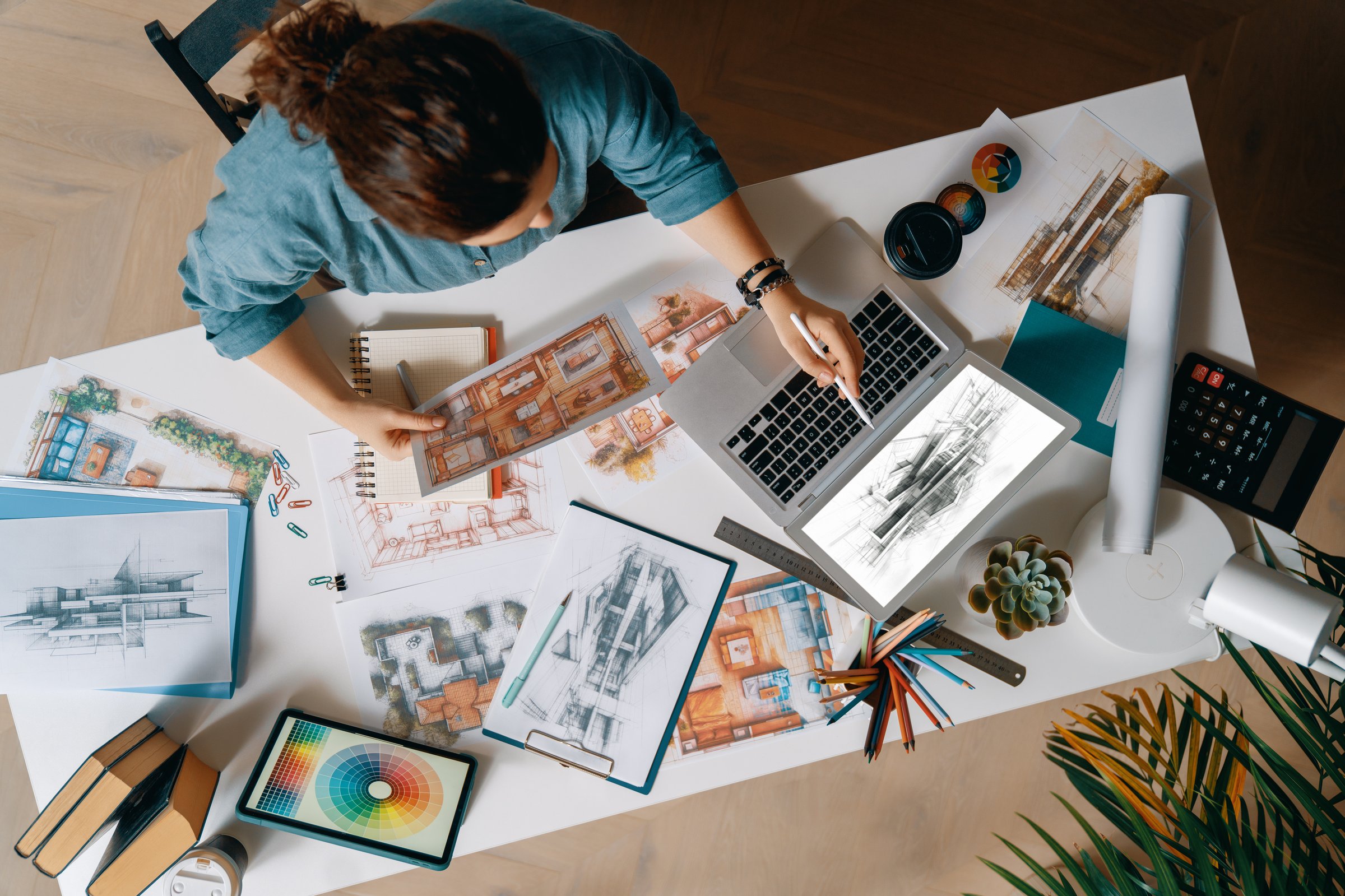 Designer working in studio and using laptop and sketches.