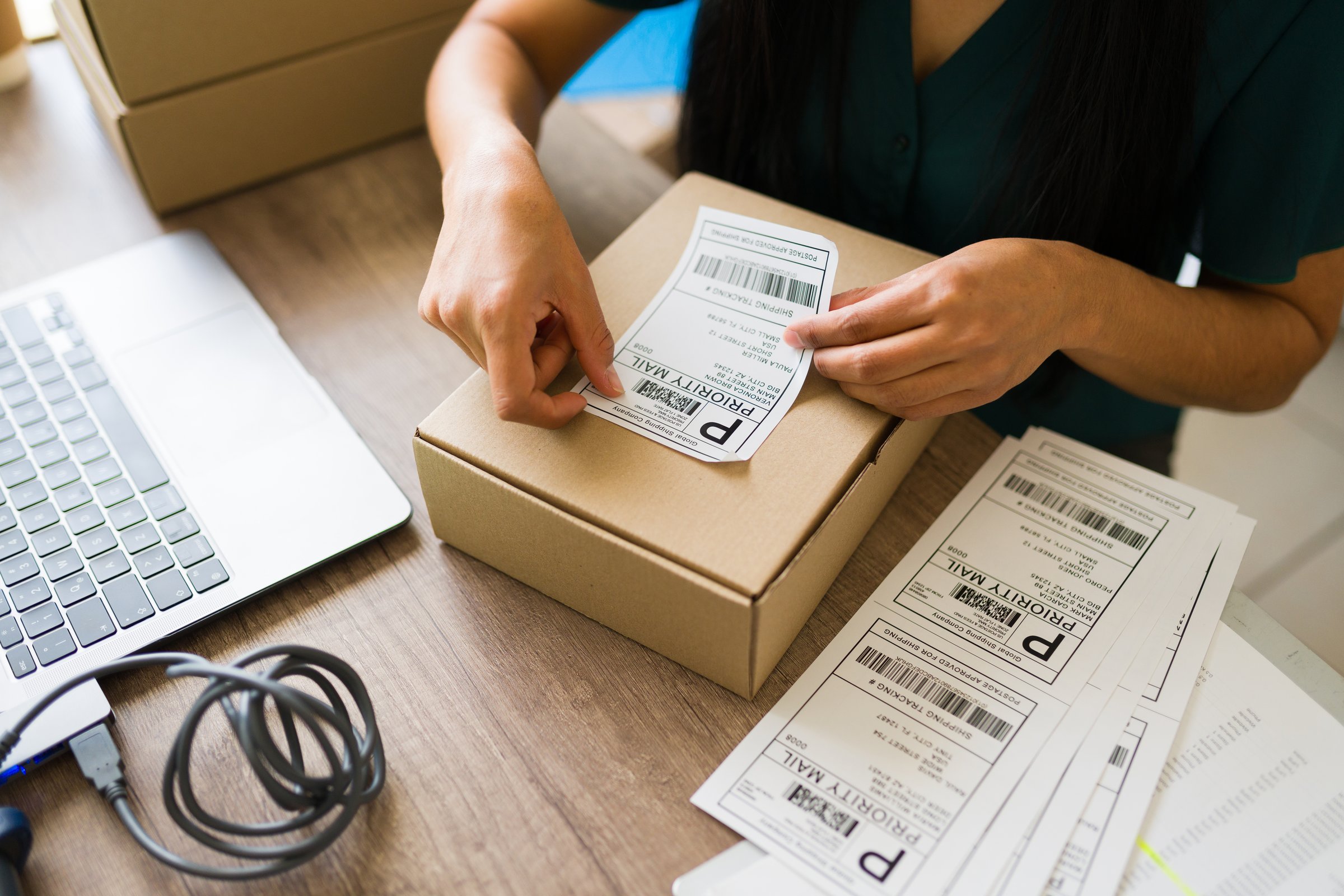 Latin woman preparing a package for shipping, sticking priority mail label on a cardboard box at her startup business office