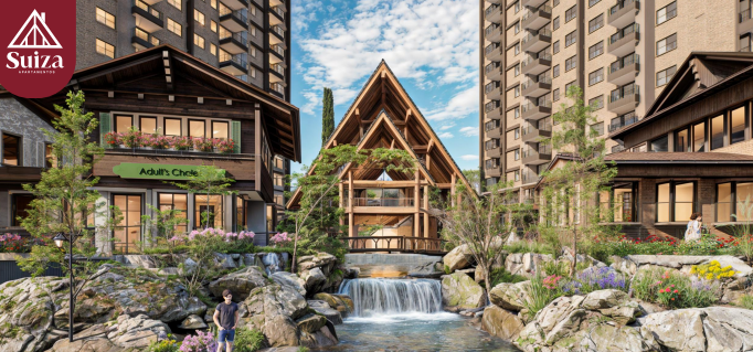 Modern residential complex with a central lodge, water feature, and landscaped gardens under a partly cloudy sky.