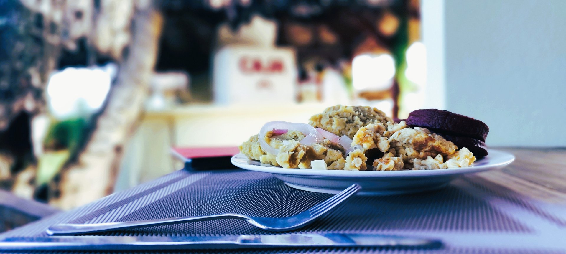 Side view of a plate with fluffy scrambled eggs topped with pickled onions and purple plantain patties on a placemat