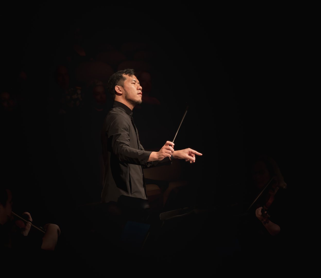 Asian-American conductor conducting classical music concert; his face is expressive