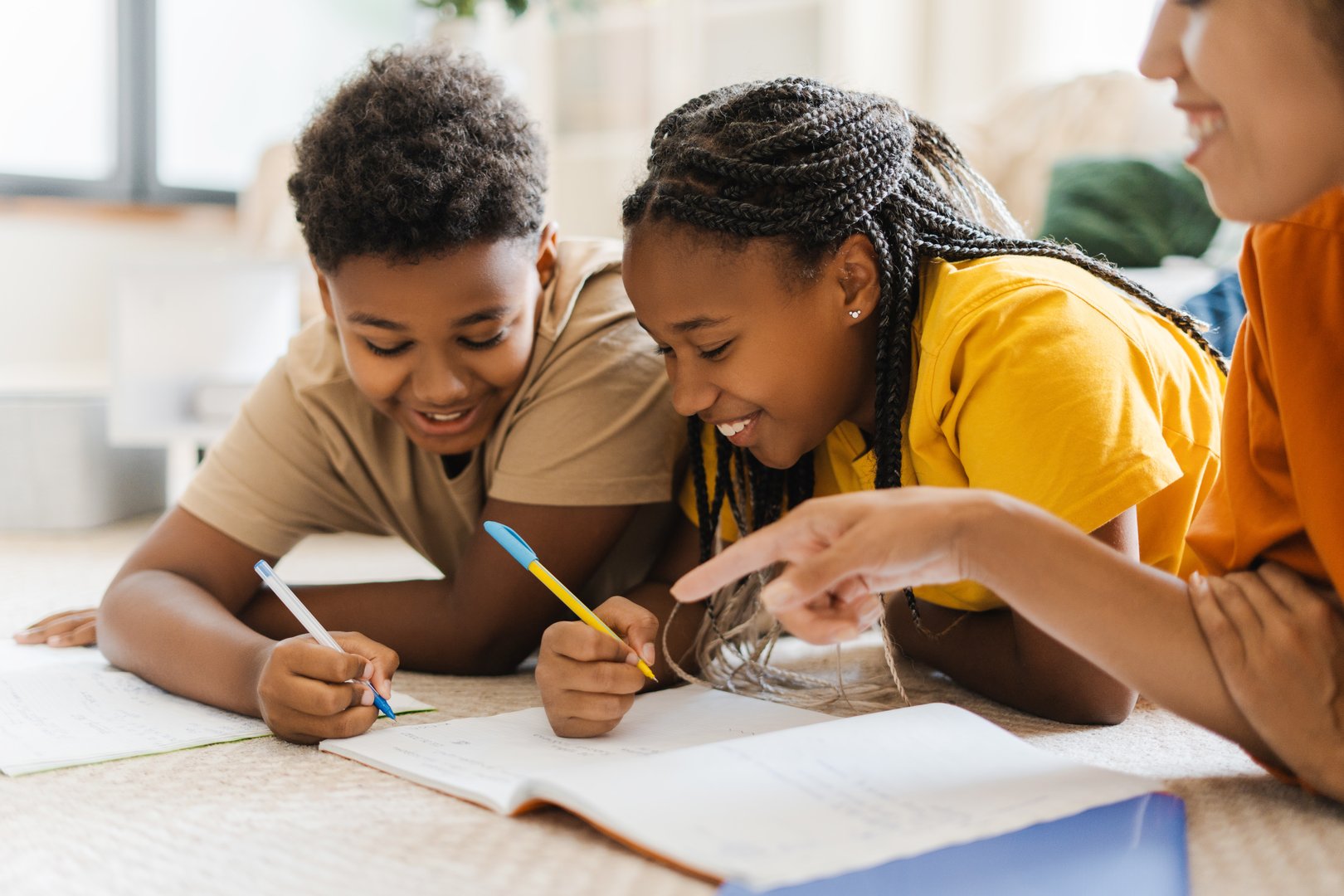 Cheerful woman and kids drawing at home at the carpet. Smiling children and parent lying at the floor together. Hobby concept