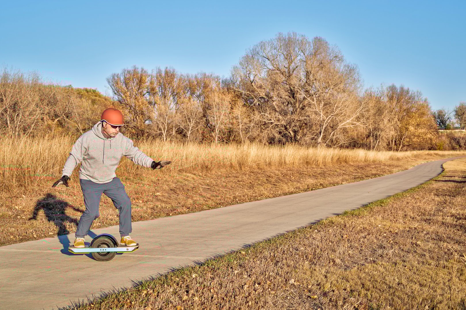 senior man is riding one-wheeled electric skateboard on a paved bike trail in fall scenery in Colorado