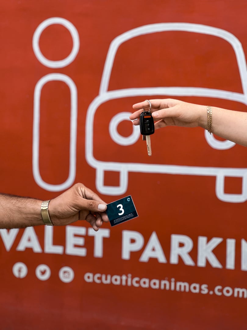 Close-up of two hands exchanging car keys and a ticket, with a red valet parking sign in the background.