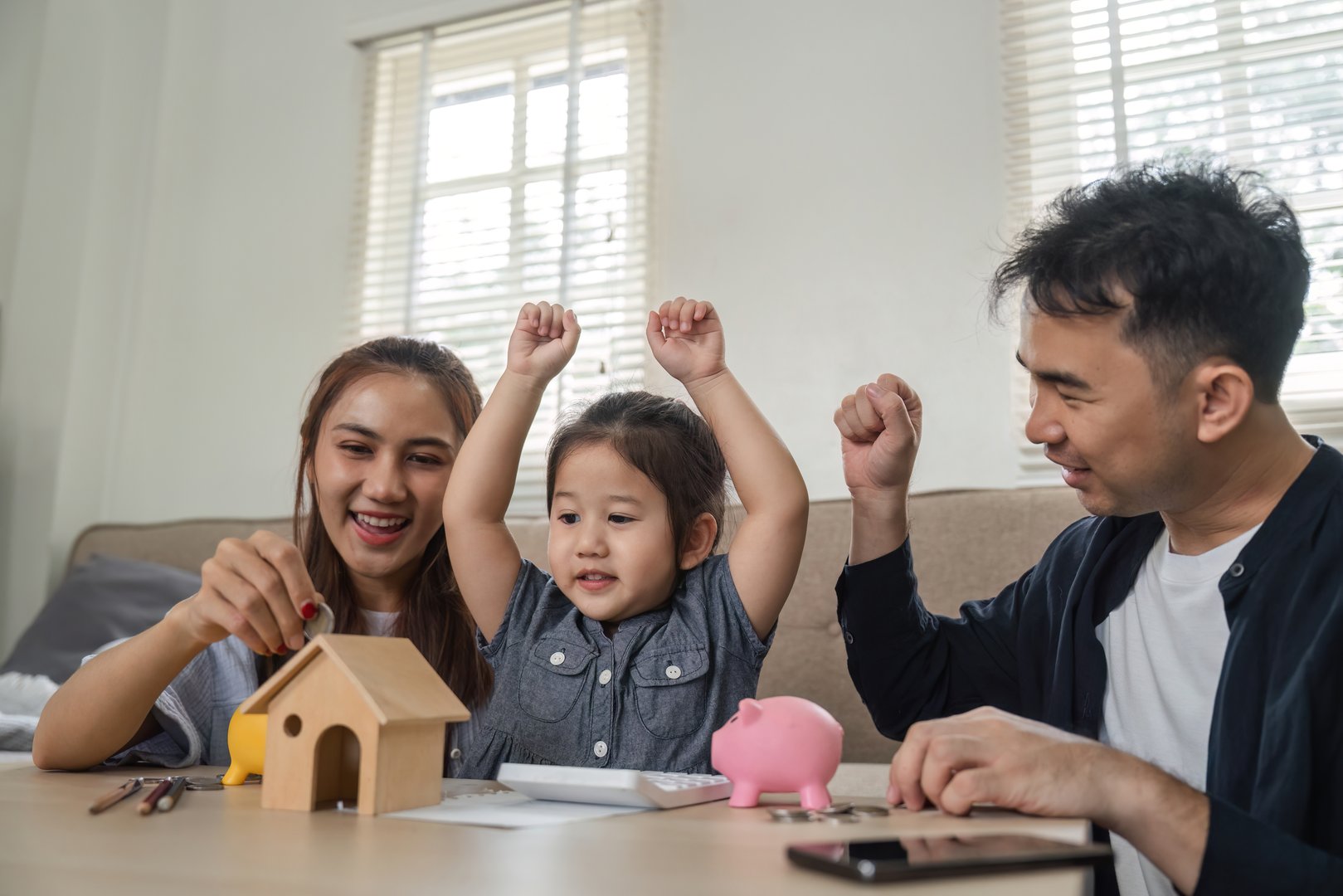 A family engages in playful learning about saving money with piggy banks, enhancing financial literacy for their child.
