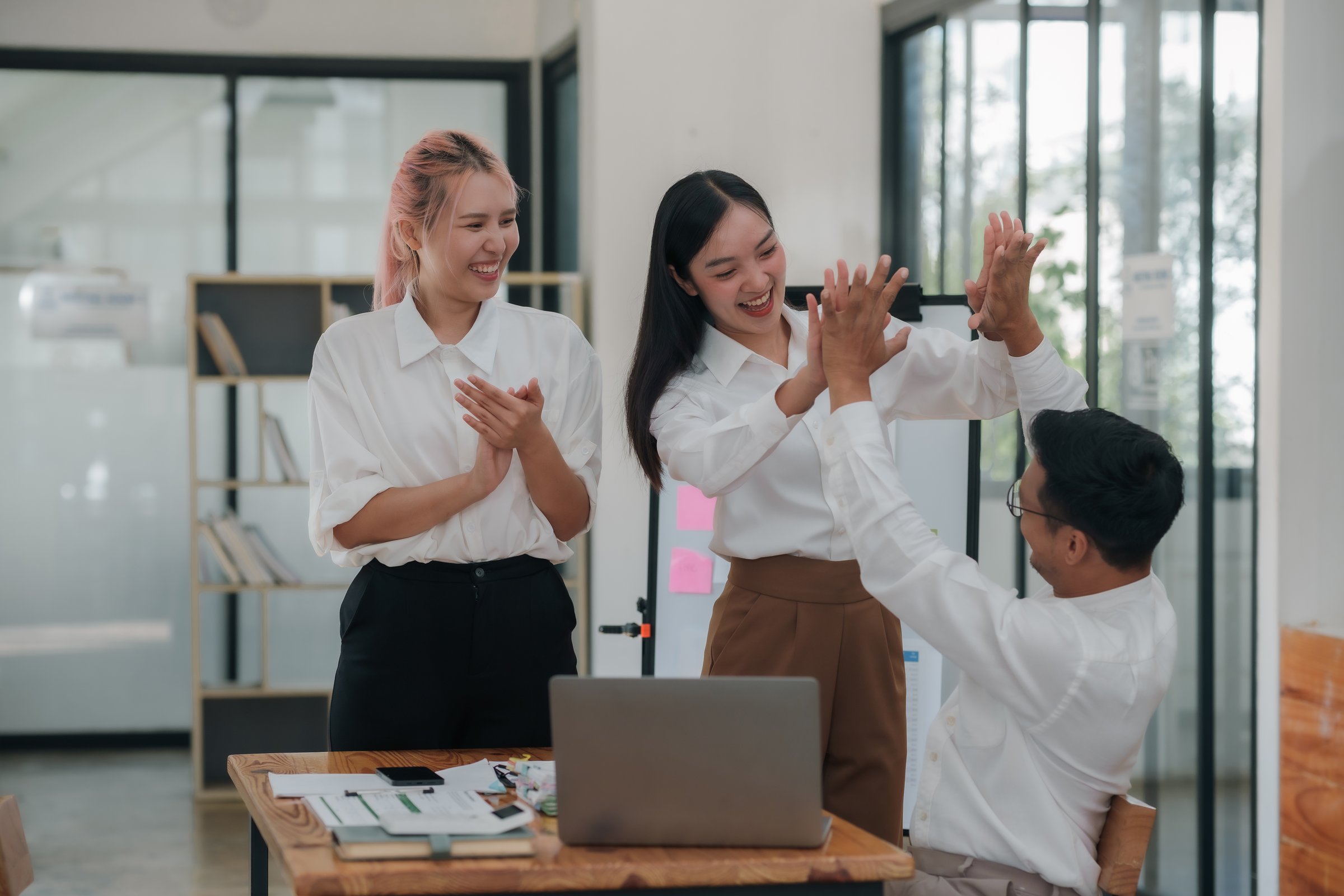 Asian business team giving high-fives in a collaborative group meeting at the office. Positive workplace culture and team success concept.