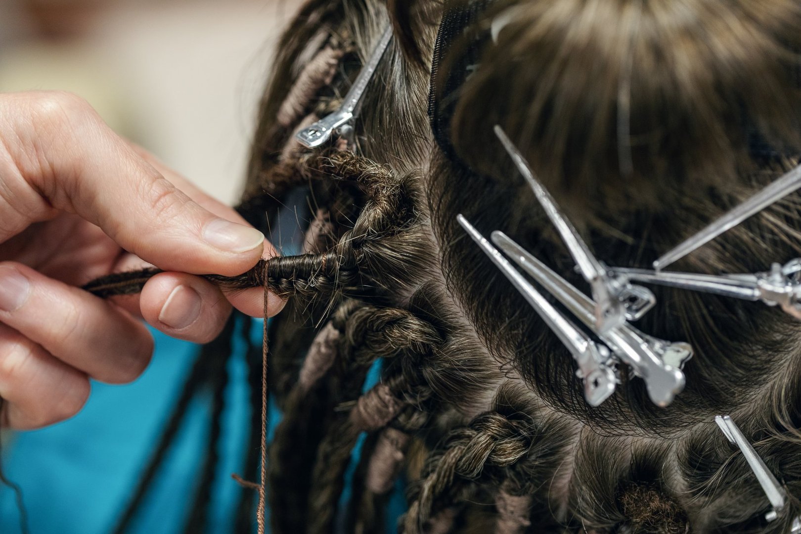 Process of braiding dreadlocks, close-up. Human dark brown hair, hairdressing clips and hairdressers fingers at work, selective focus. Barbershop, expert, skill, service, lifestyle concept.