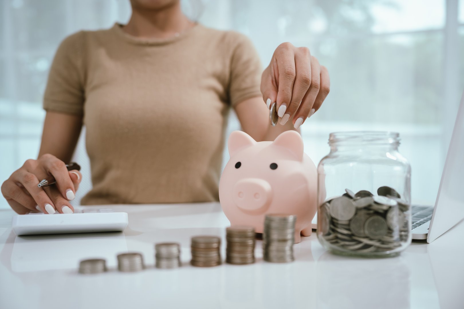 An Asian woman plans to divide her money into coins and a piggy bank, symbolizing budgeting, financial planning, saving, and smart money management.