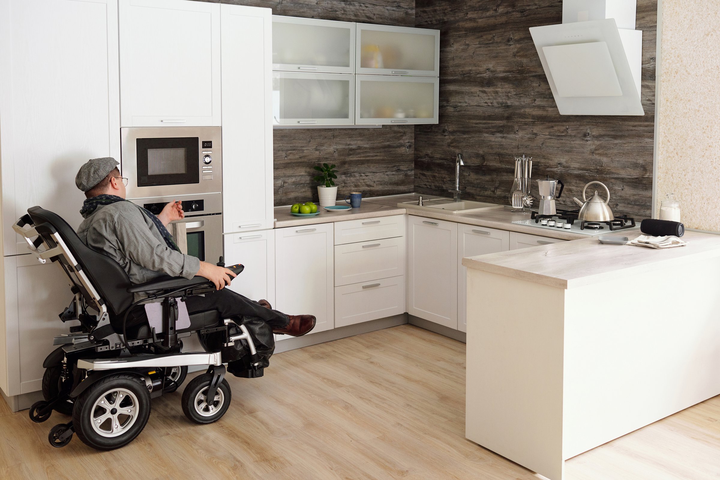 Middle aged man with disability sitting by electric oven in large comfortable kitchen in home environment