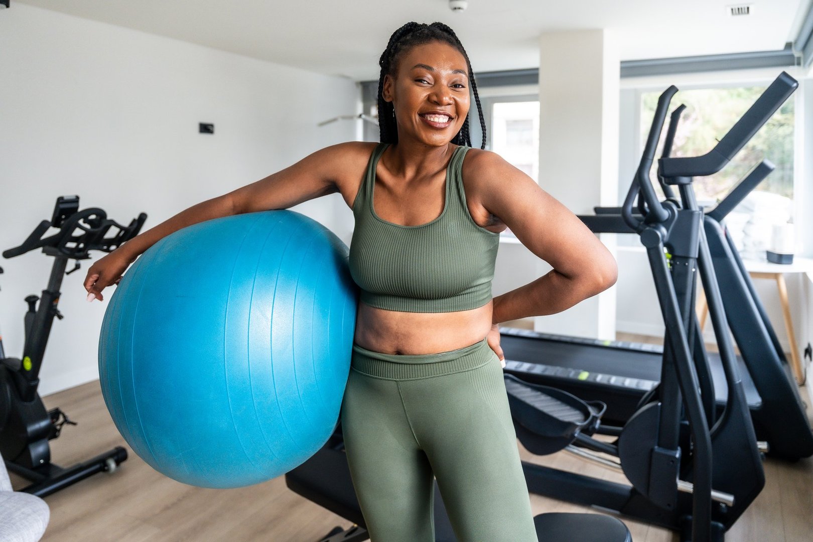 Confident young woman smiling while holding a fitness ball during her workout in a hotel gym, promoting a healthy lifestyle during business trips