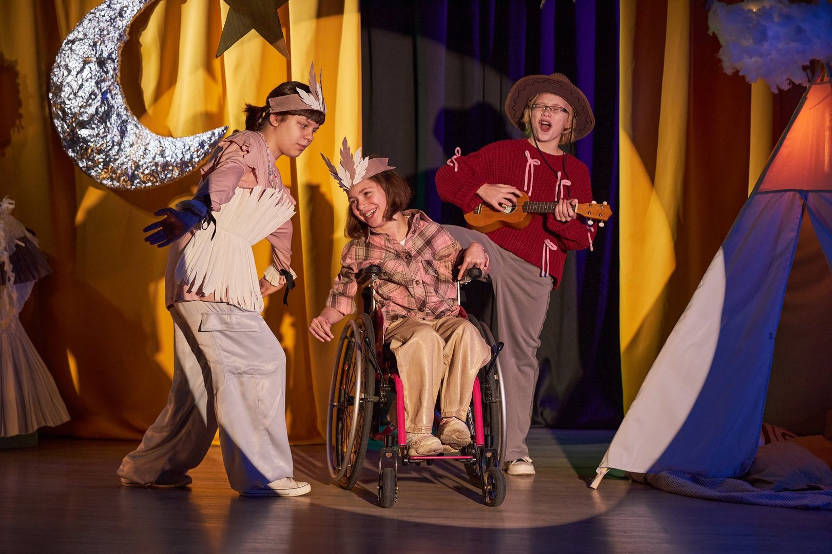 Full length of three perky young singers performing country song on stage, participating in Western musical play at inclusive childrens theater while standing in bright spotlight