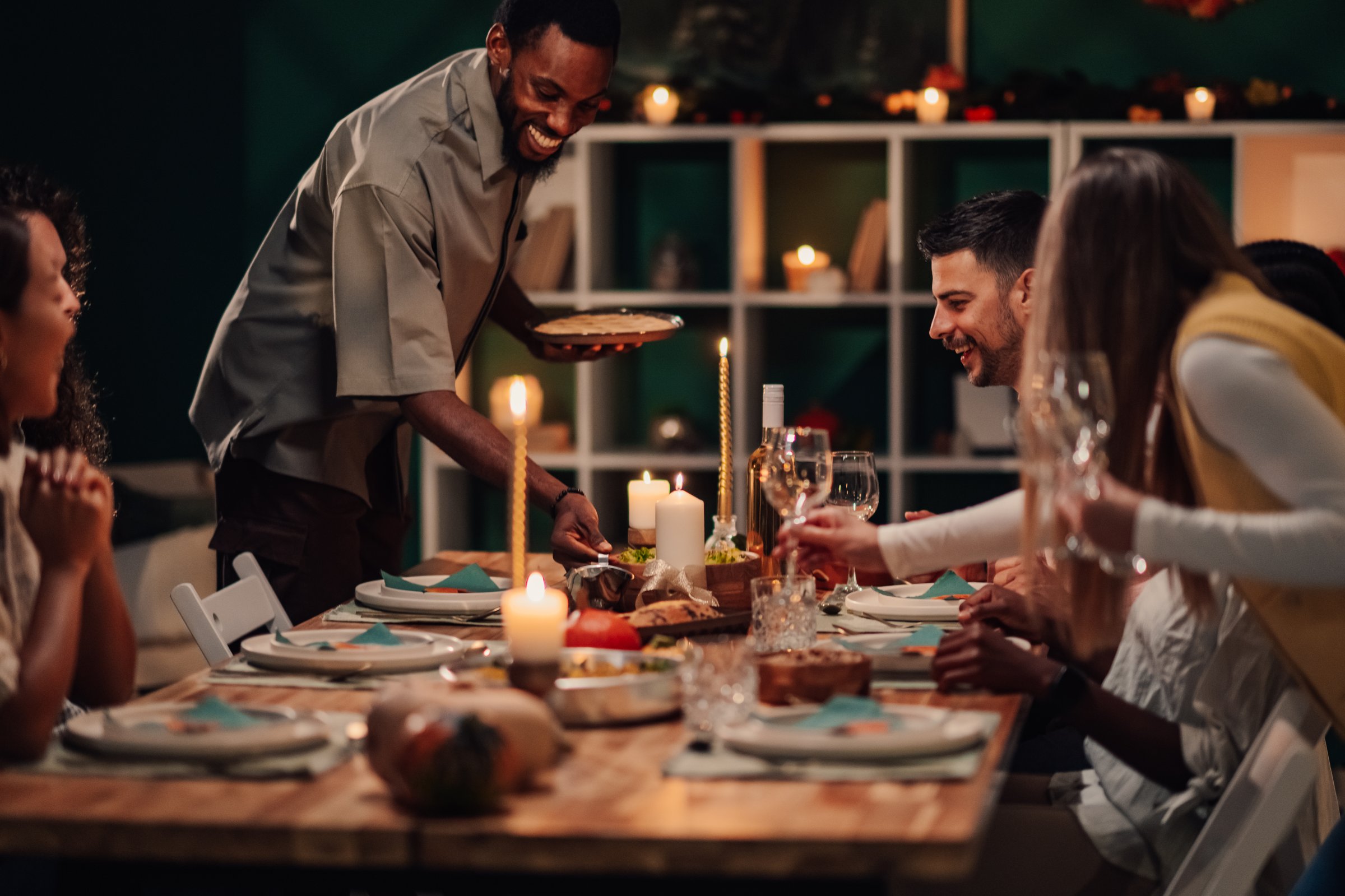 Friends are gathering around a beautifully set table, enjoying a festive dinner with delicious food, drinks, and warm candlelight