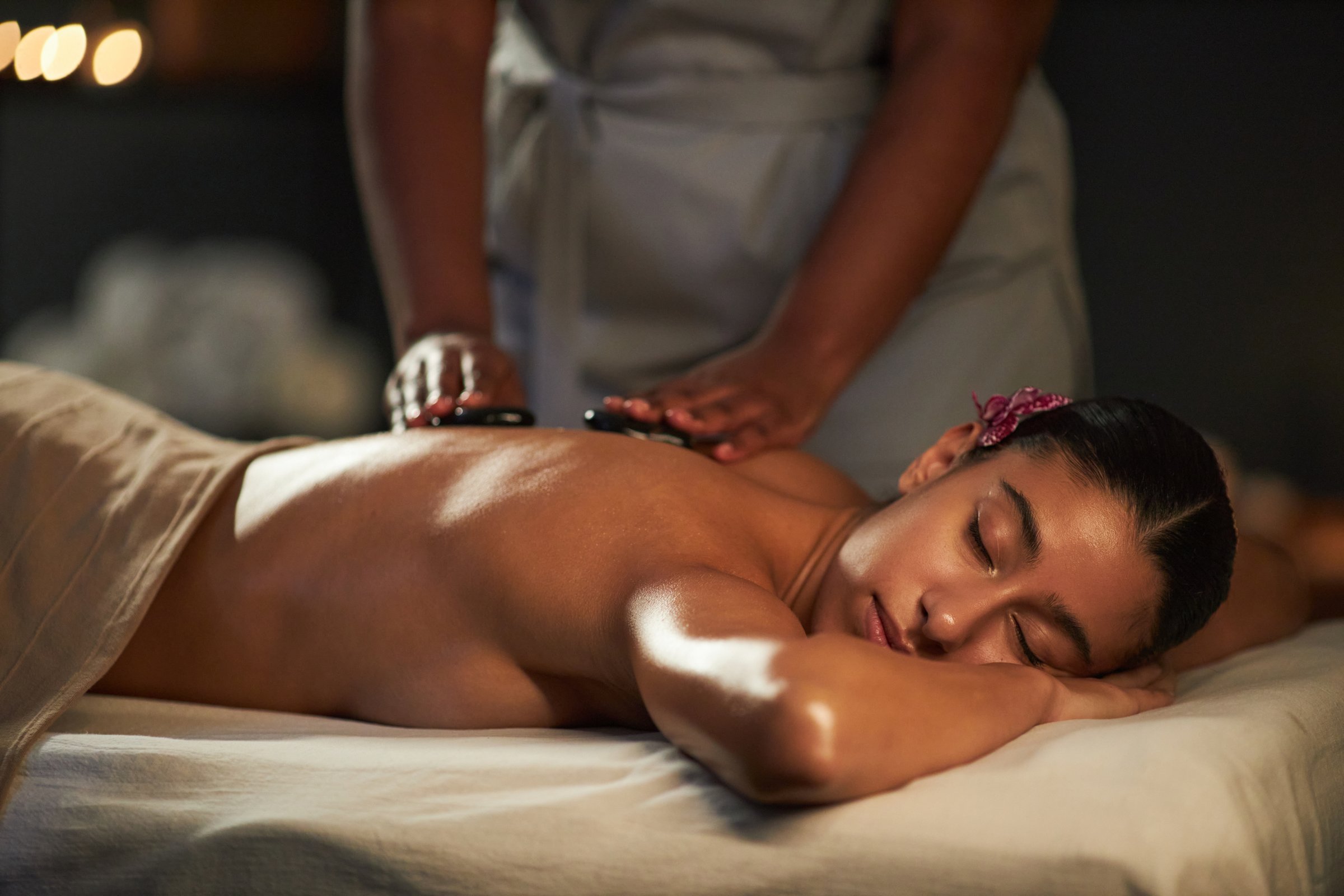 Woman relaxing on massage table while getting therapeutic back massage by masseuse in serene spa environment, soft lighting creating calm, peaceful atmosphere