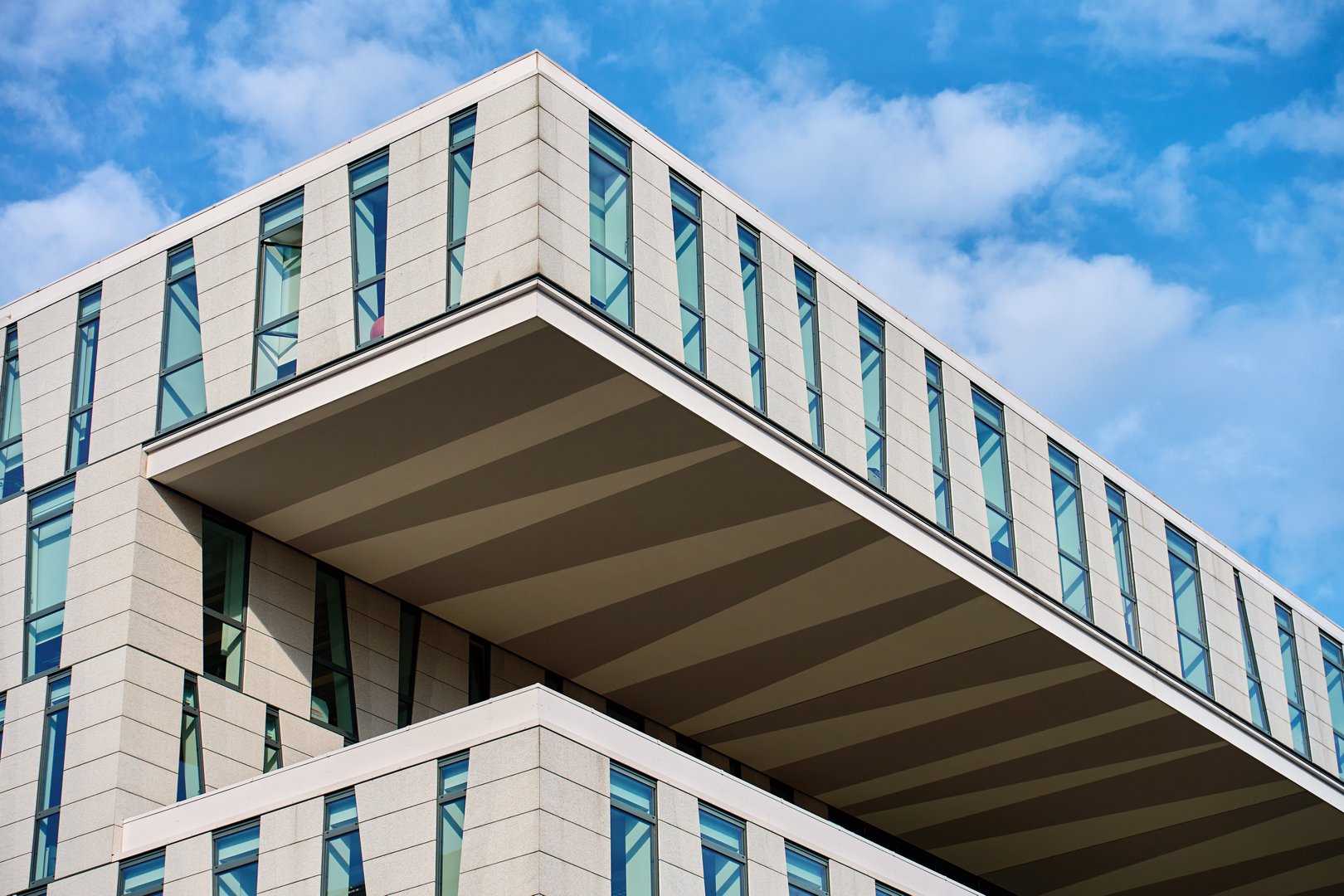 Modern stacked facade of an urban building with glass windows and concrete panels under blue sky. Contemporary city architecture with geometric lines in brutalism style
