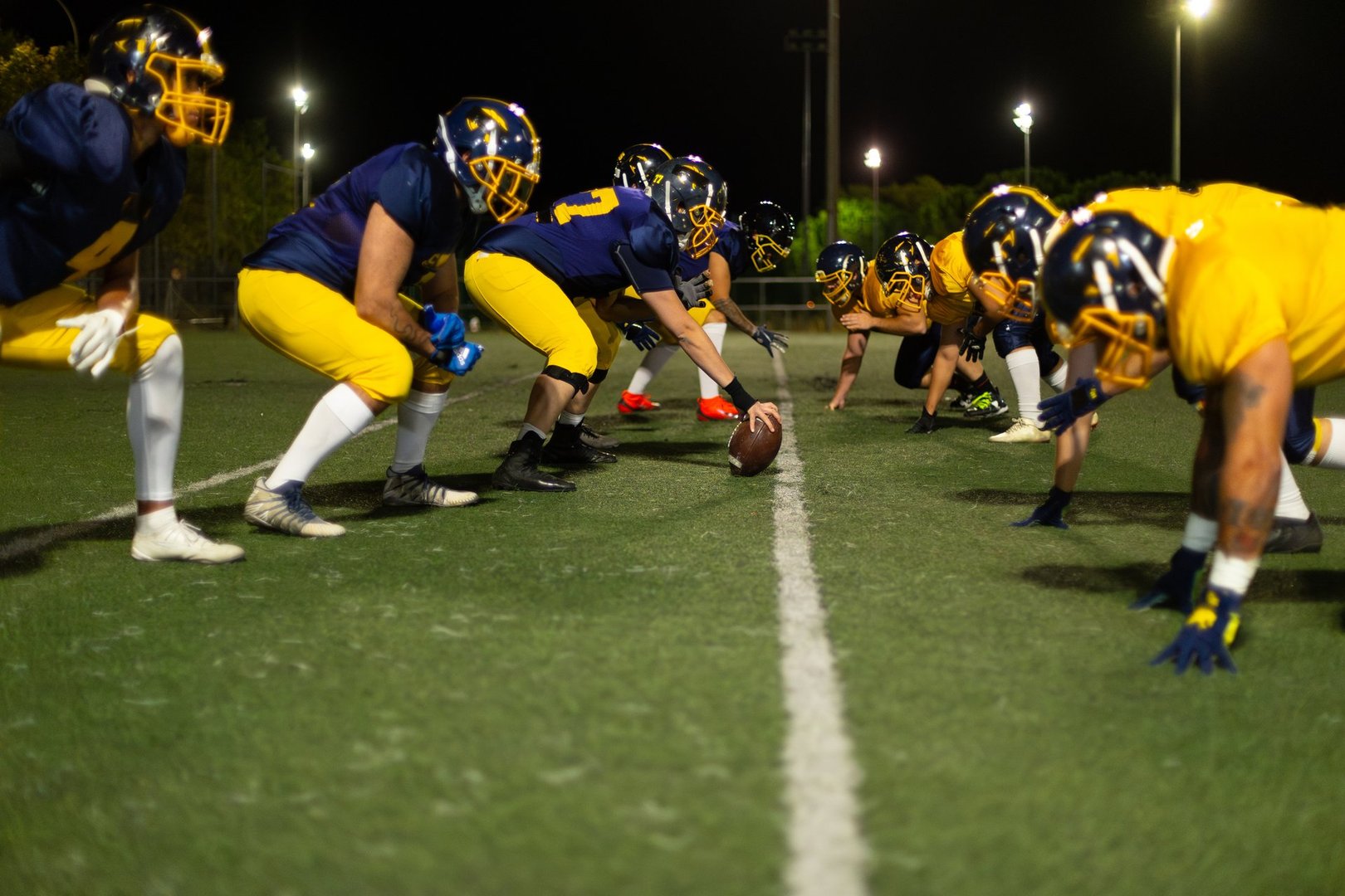 American football players taking position at the line of scrimmage, preparing to start a play on the illuminated field