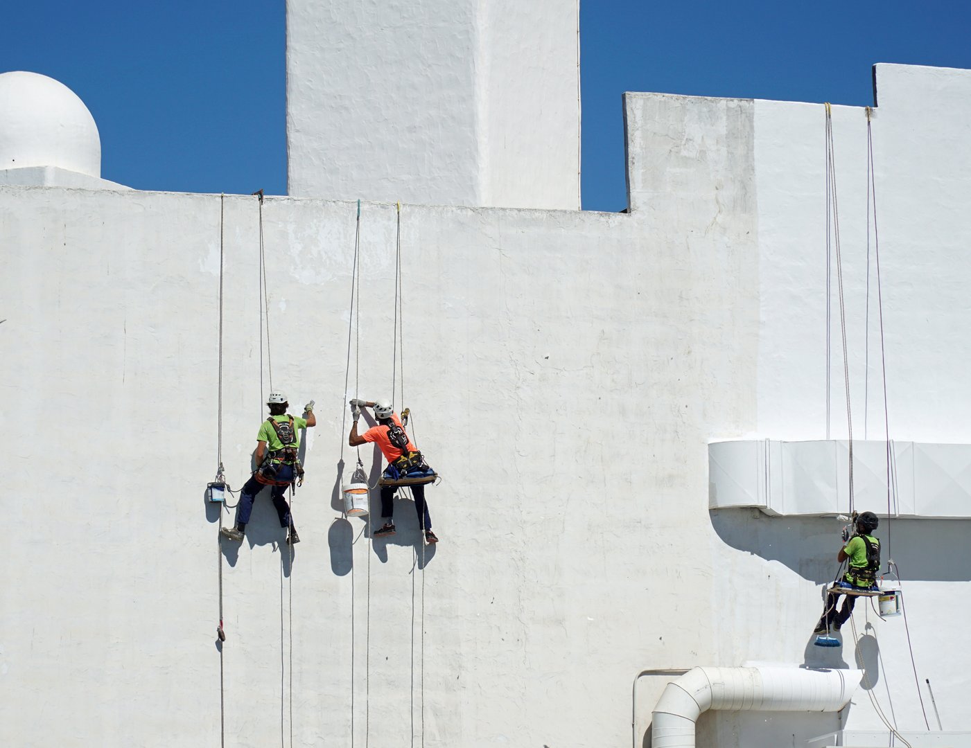 Playa Blanca, Lanzarote, Spain - October 11, 2024:  Three Abseiling painters painting white wall