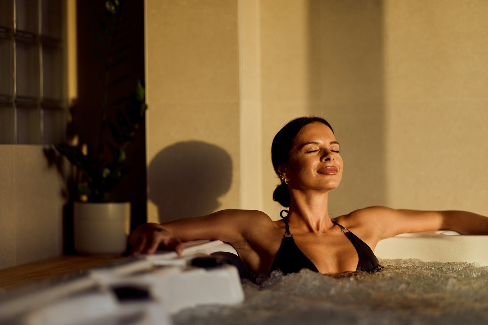 Woman enjoying relaxation in a modern spa's hot tub under soft, serene lighting.