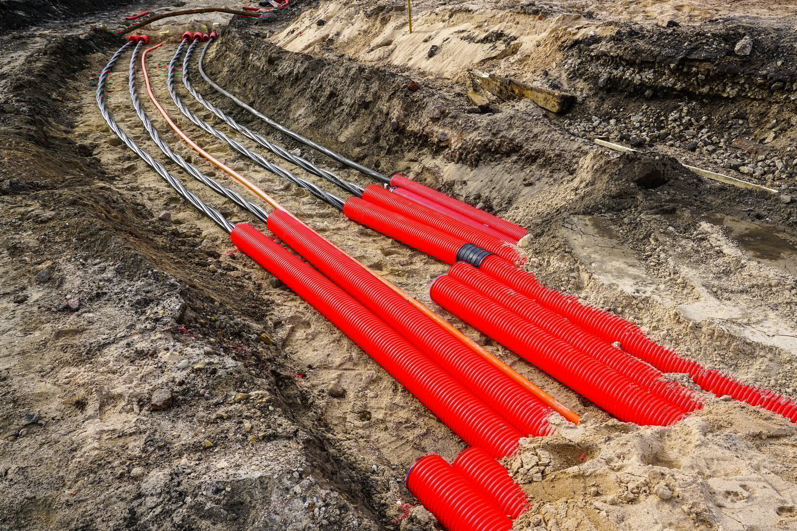 Laying a new underground high-voltage power cable in red corrugated protective tube for the power supply of an industrial facility, cable installation