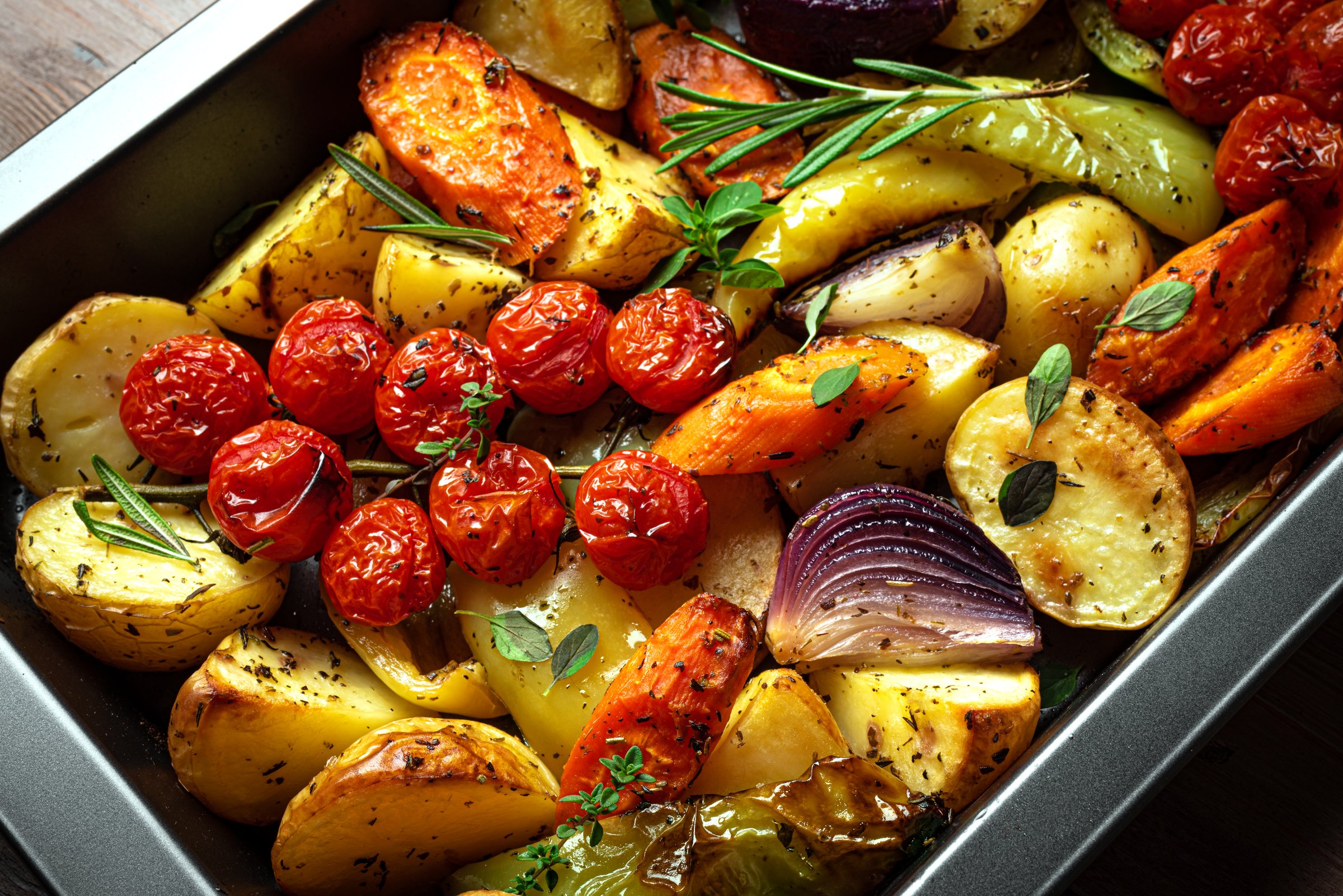 Autumn meal: oven roasted seasonal vegetables with garlic and herbs on baking tray close up. Oven baked veggies, vegan food or side dish.