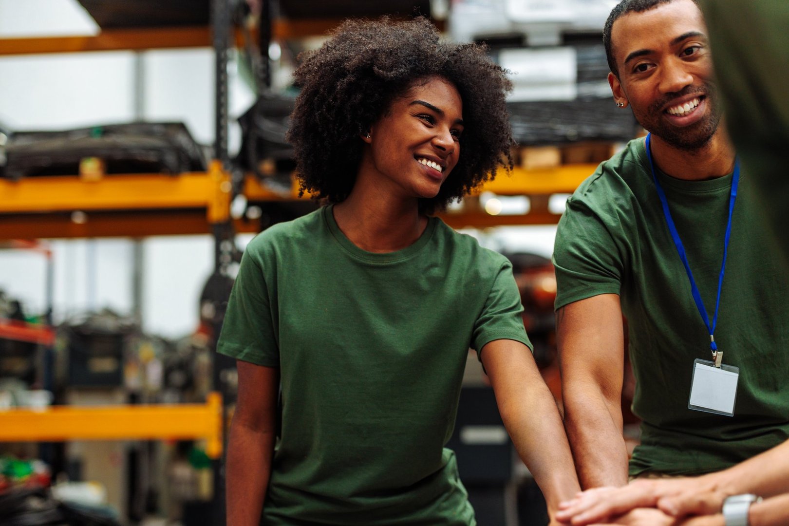Happy volunteers wearing matching t-shirts stacking hands together, smiling, and working as a team in a warehouse