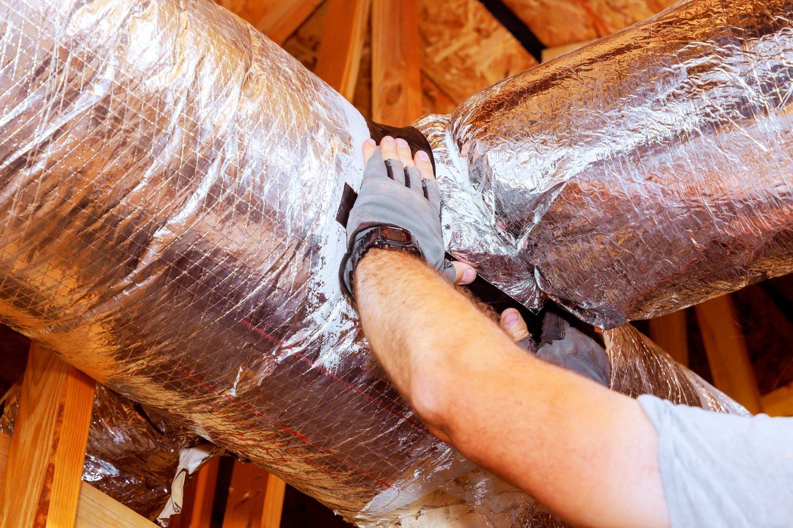 Contractor worker adjusts insulation around ductwork in residential attic, ensuring proper sealing efficiency.
