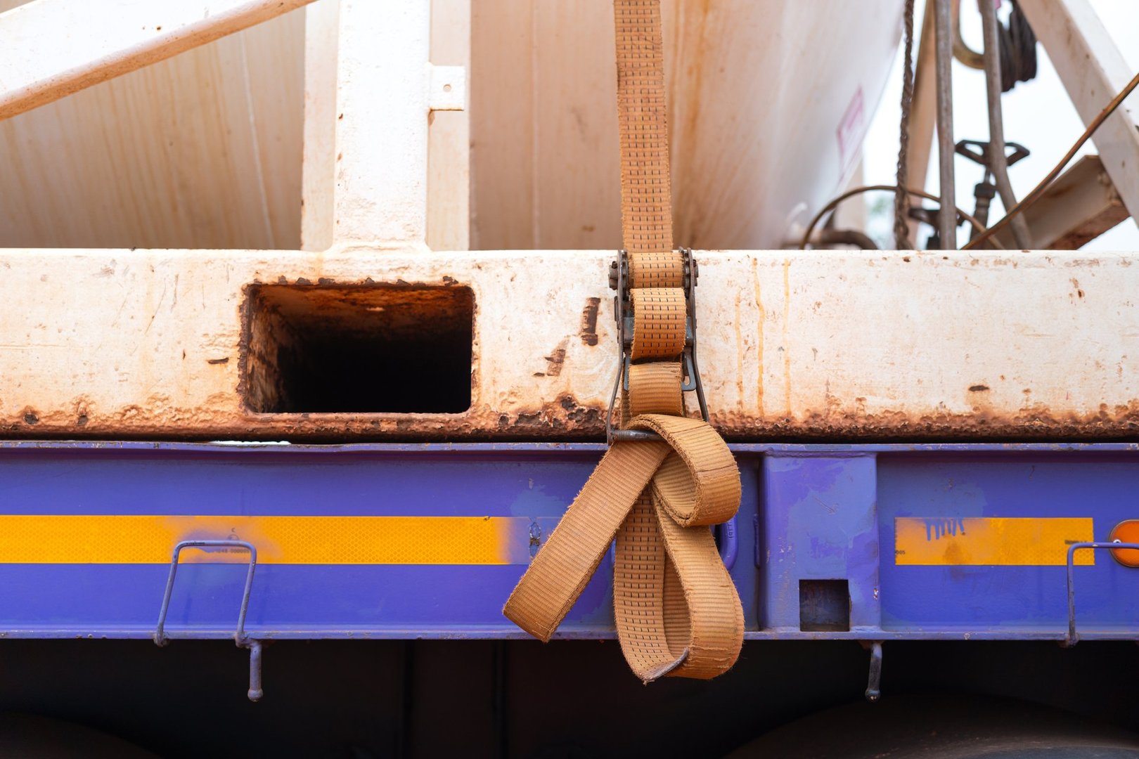 Latching belt strap with metal buckle that securing heavy load on trailer truck to prevent object falling during transportation. Close-up and selective focus.