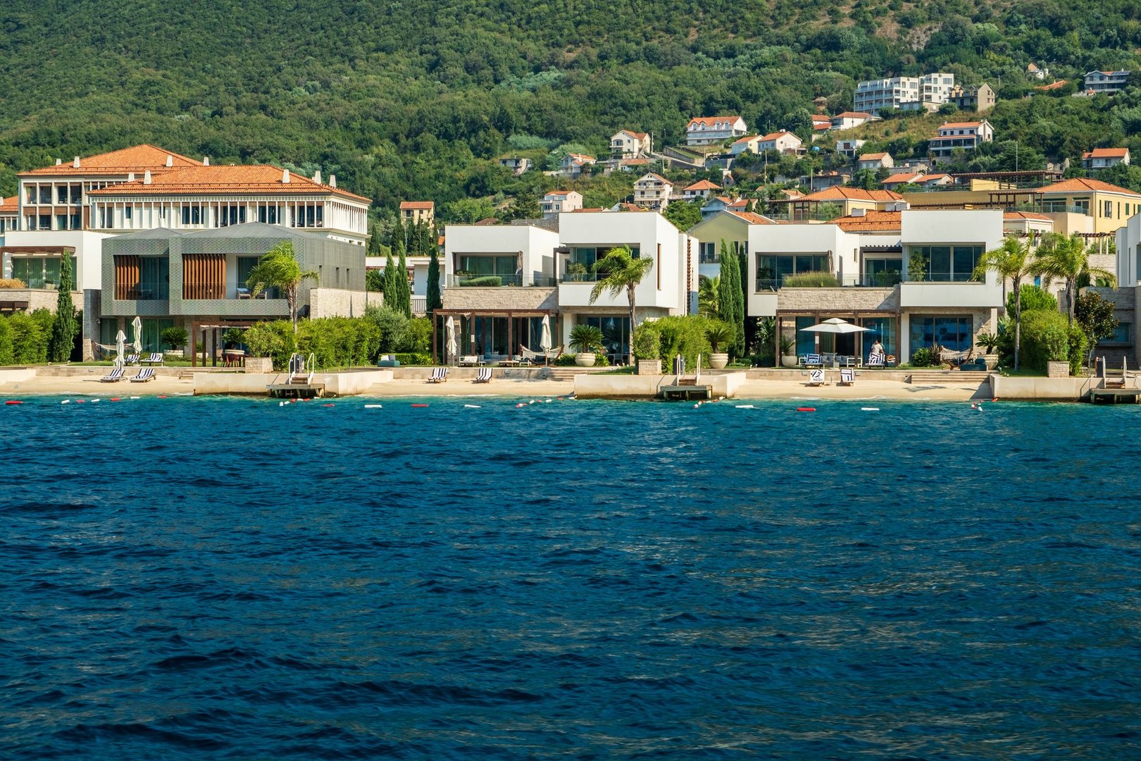 Luxury beachfront villas featuring modern architecture, private beach access, and stunning sea views, set against a lush hillside backdrop.