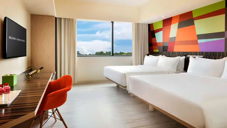 Modern hotel room with two beds, colorful geometric wall art, a desk with a chair, and a large window with a view.