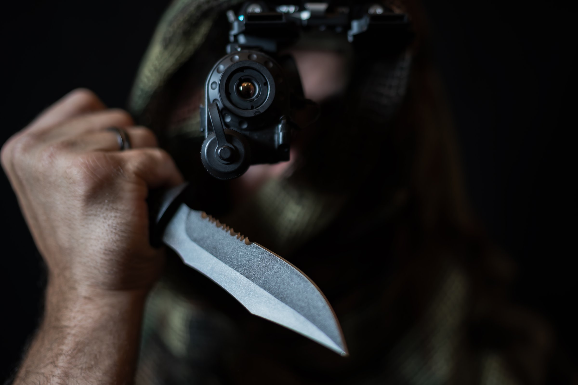 A reconnaissance warrior in camouflage, with a night vision device and a sharp knife in his hand. Photo with soft focus.