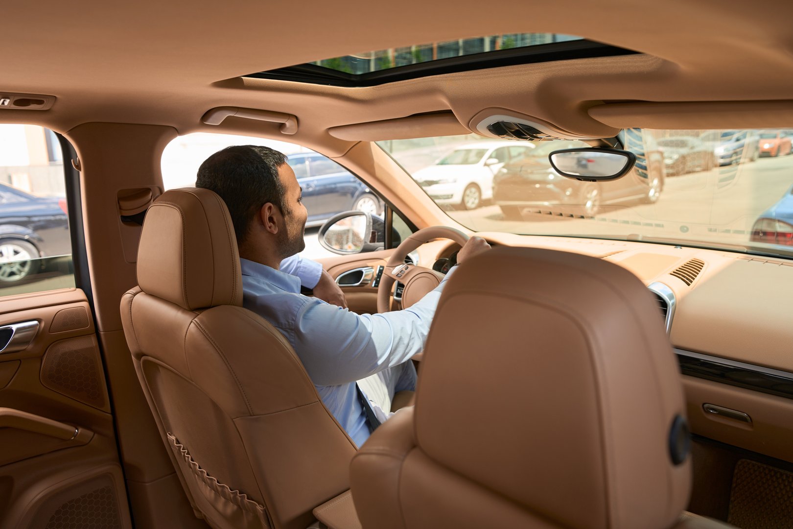 Male seated in front seat of luxury car with one hand on steering wheel