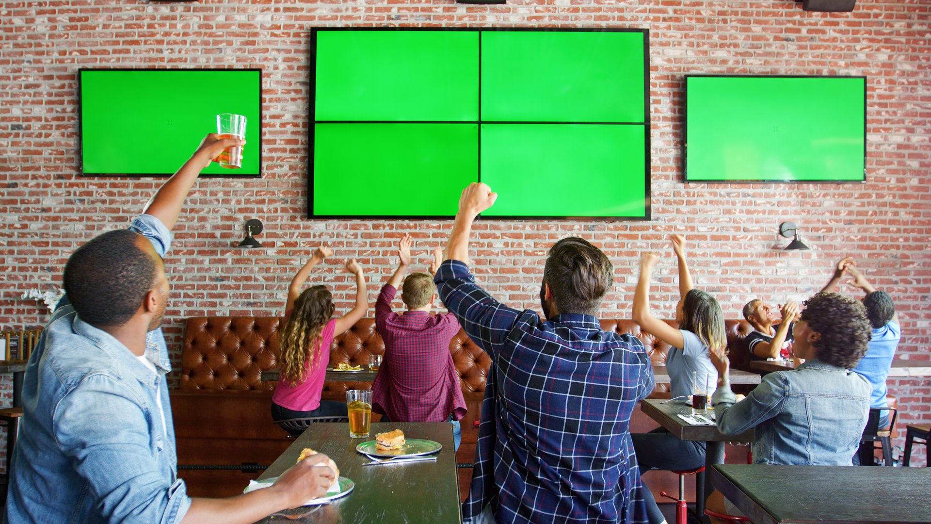 People Sitting At Tables In Sports Bar Watching Game On Green Screens And Celebrating