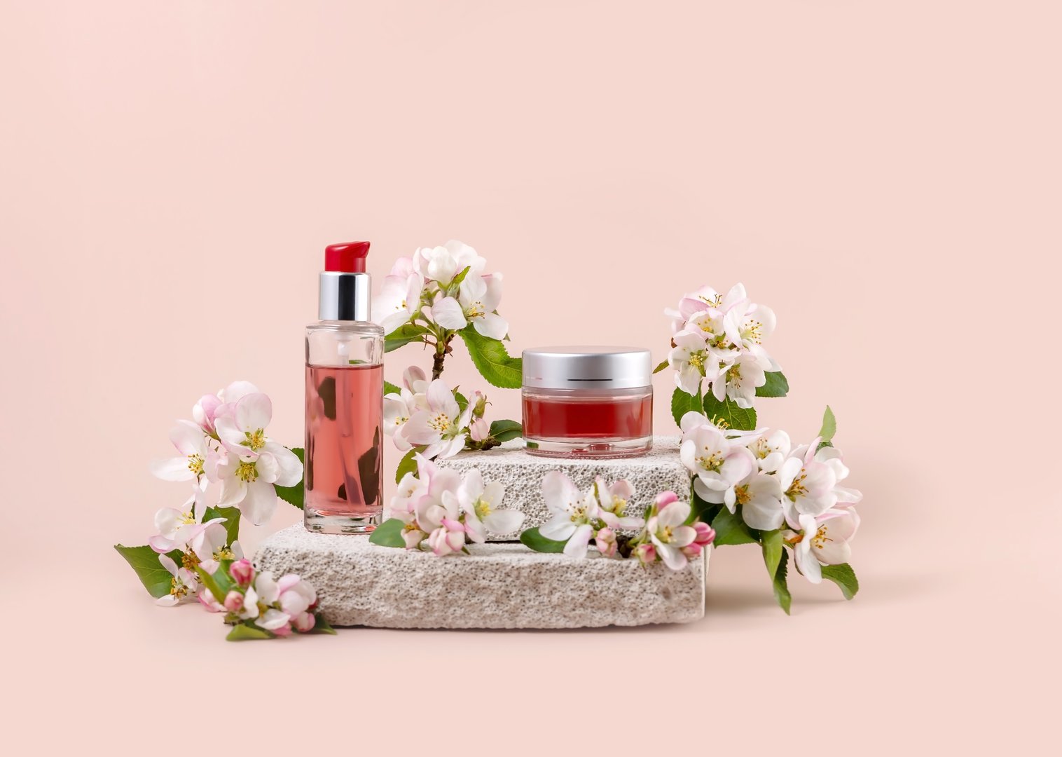 cosmetics containers on a stone catwalk and branches of a blooming apple tree on a pink background