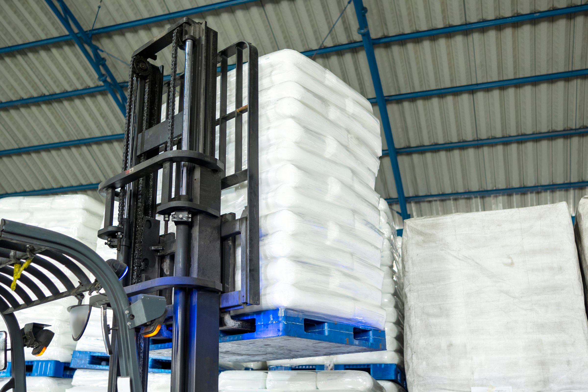 Forklift lifts a stacked white sack in a warehouse. Storage, inventory, industry, and logistics