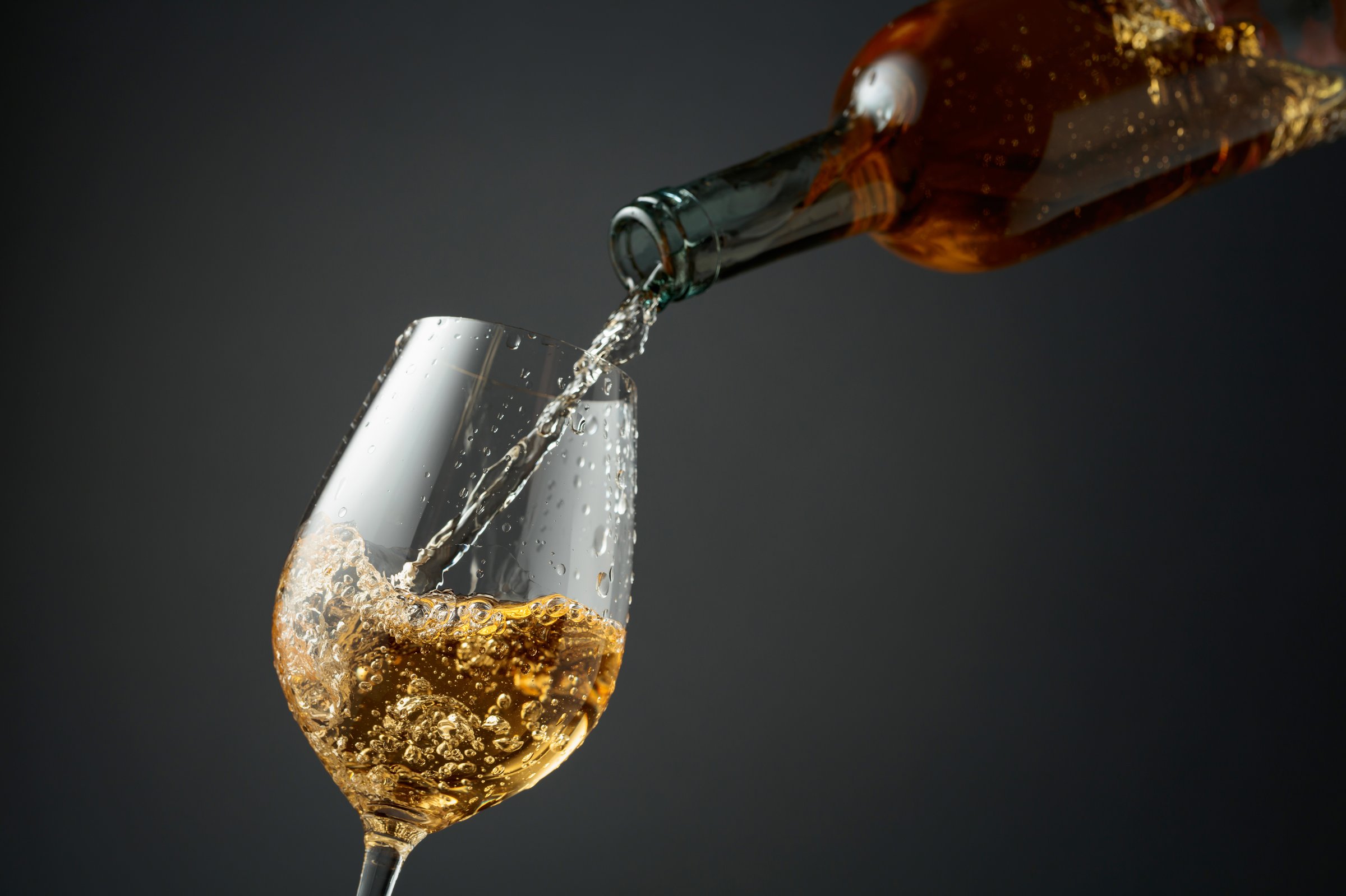 Pouring white wine from a bottle into a glass. Gray background with copy space.