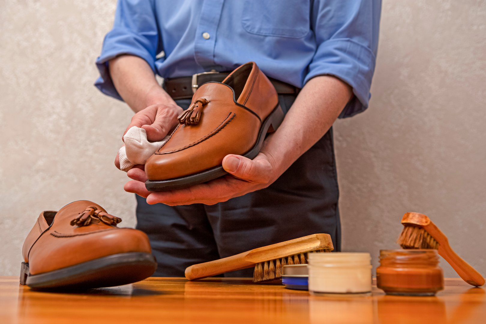 Hands of Professional Male Shoes Cleaner with Cleaning Shoe Wax, Cream and Brushes For Tan Calf Leather Tassel Loafers Shoes While Working in Workshop. Horizontal Composition Image