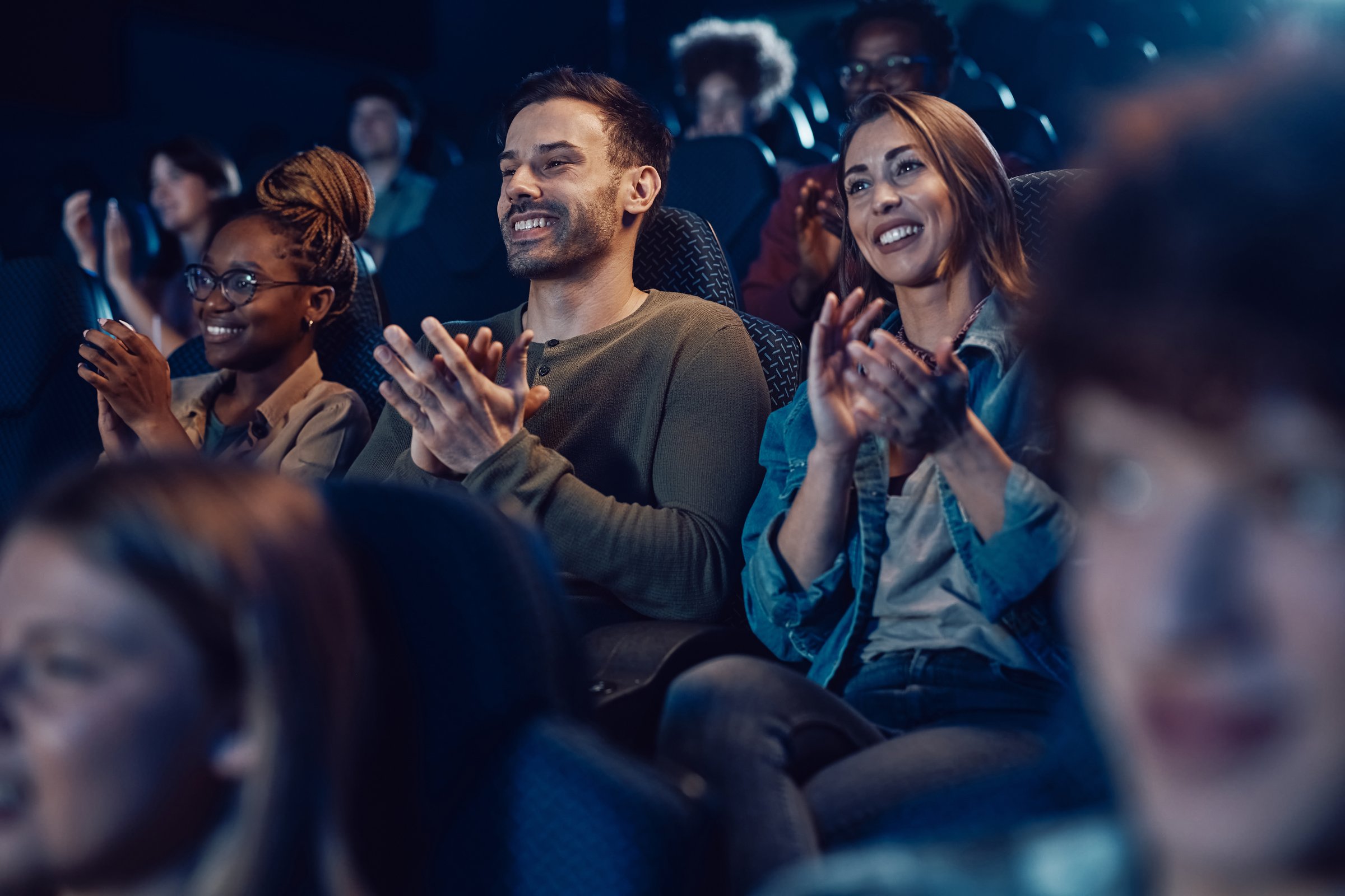 Group of happy people applauding after film screening at movie theatre.