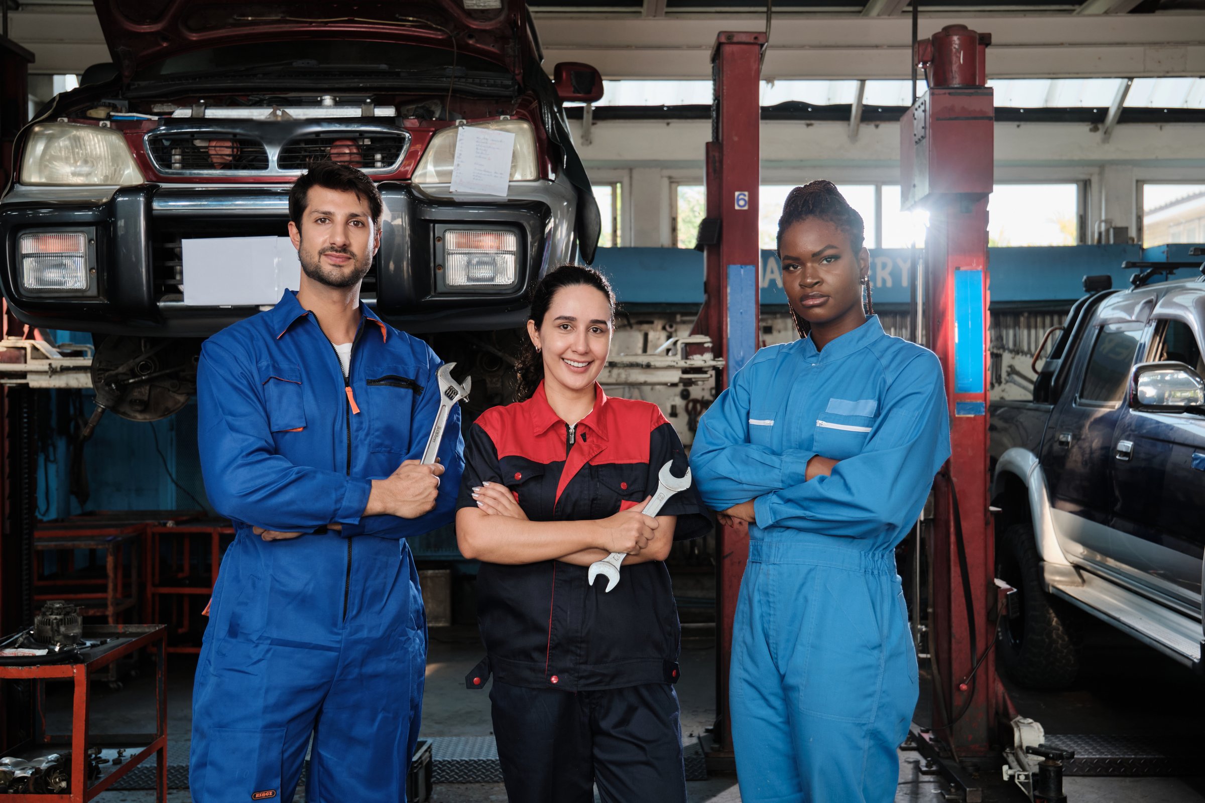 Harmonious professional mechanic teamwork, multiracial engineers are rowing, cheerful, arms crossed and smile in fix car garage, maintenance service jobs in automotive transport industry station.