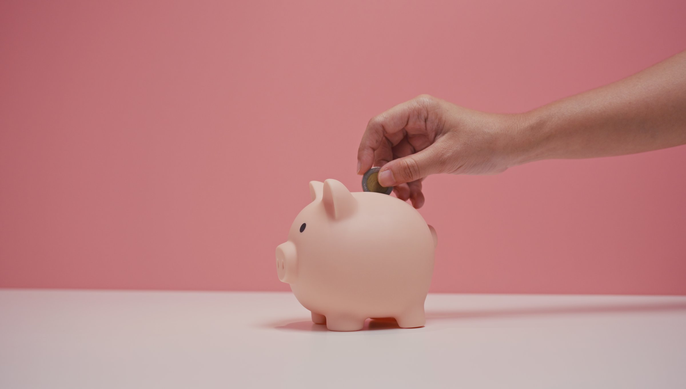 Hand dropping coin into piggy bank, charity donations concept
